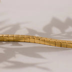 Close-up of the Cube Bracelet, a gold bracelet with geometric square links on a light surface and soft leaf shadows—a bold accessory inspired by men's statement jewelry.
