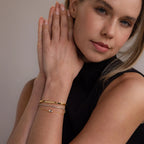 A woman in a sleeveless black top clasps her hands, highlighting gold and silver bracelets on her wrist, including the striking Cube Bracelet featuring geometric bead links.