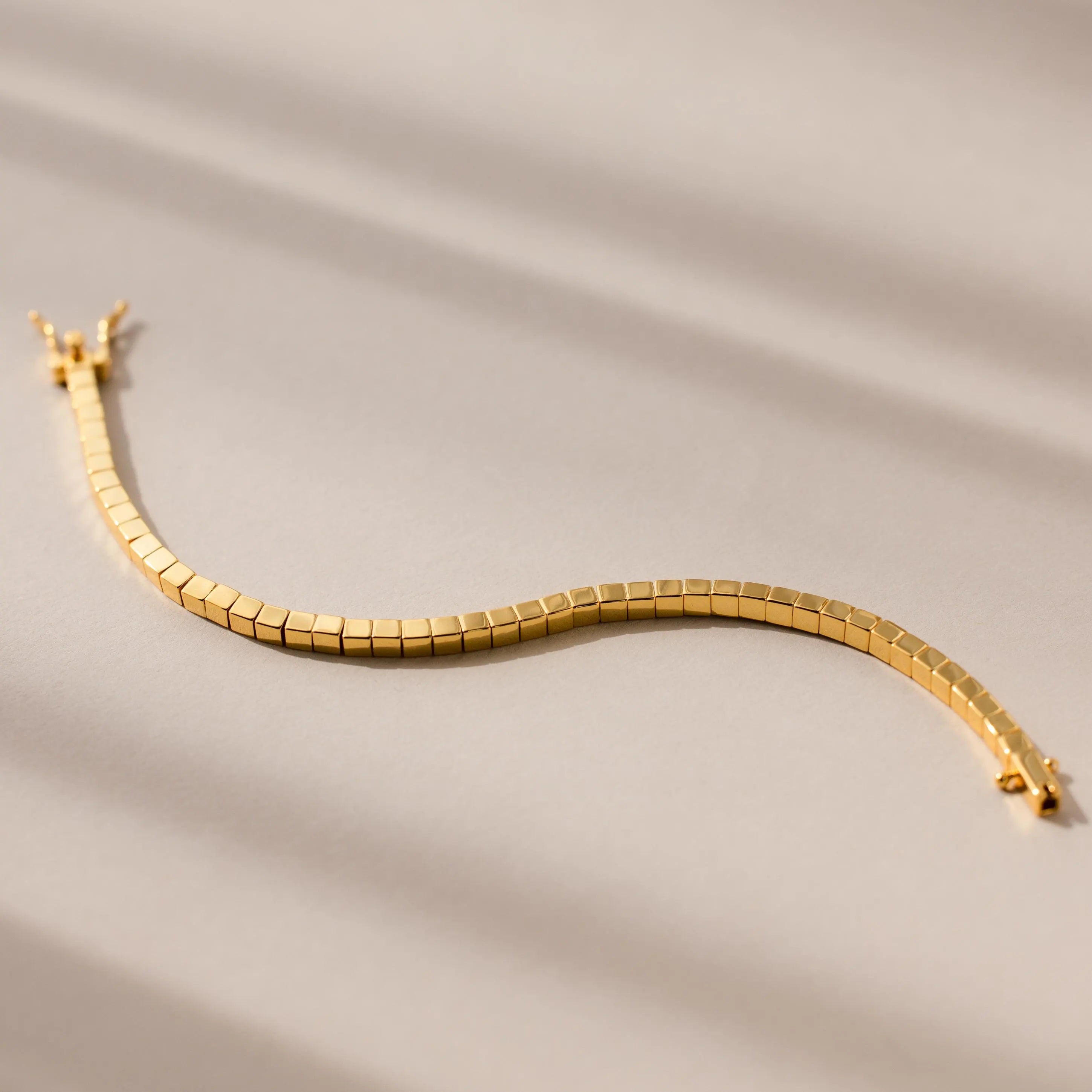 The Cube Bracelet showcases geometric bead links with a wavy design, displayed on a neutral beige background—an ideal statement piece for men.