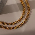 A Strap Bracelet with a gold textured link design rests on a beige surface under soft lighting—an elegant statement piece.