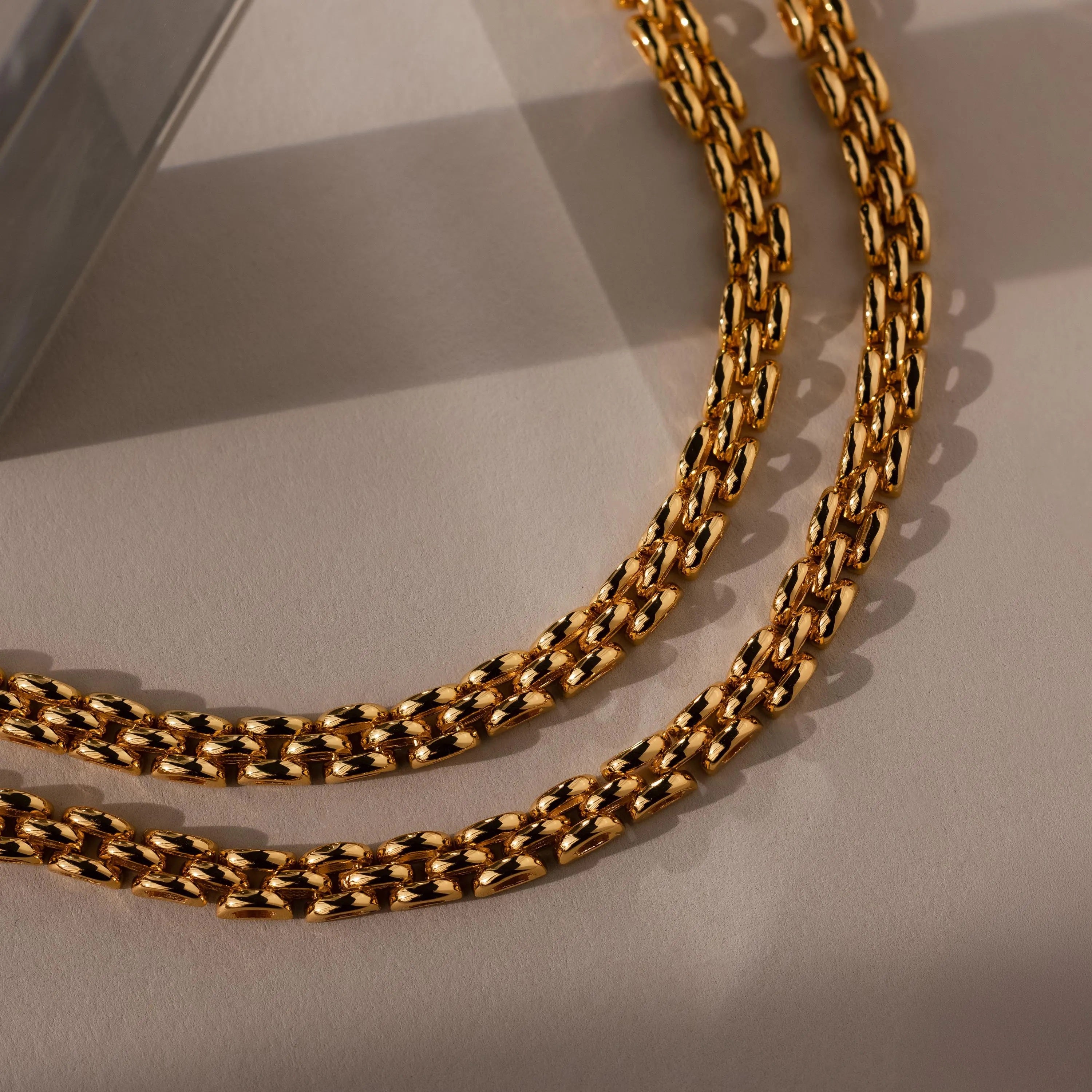 A Strap Bracelet with a gold textured link design rests on a beige surface under soft lighting—an elegant statement piece.