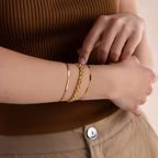 A person wears a brown ribbed top with beige pants, accessorized with three gold bracelets—one of them is the bold Strap Bracelet, serving as a statement piece.