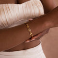 A woman wears the Bold Mariner Chain Bracelet with oversized links and an off-white, pleated strapless top—a perfect statement accessory for any occasion.