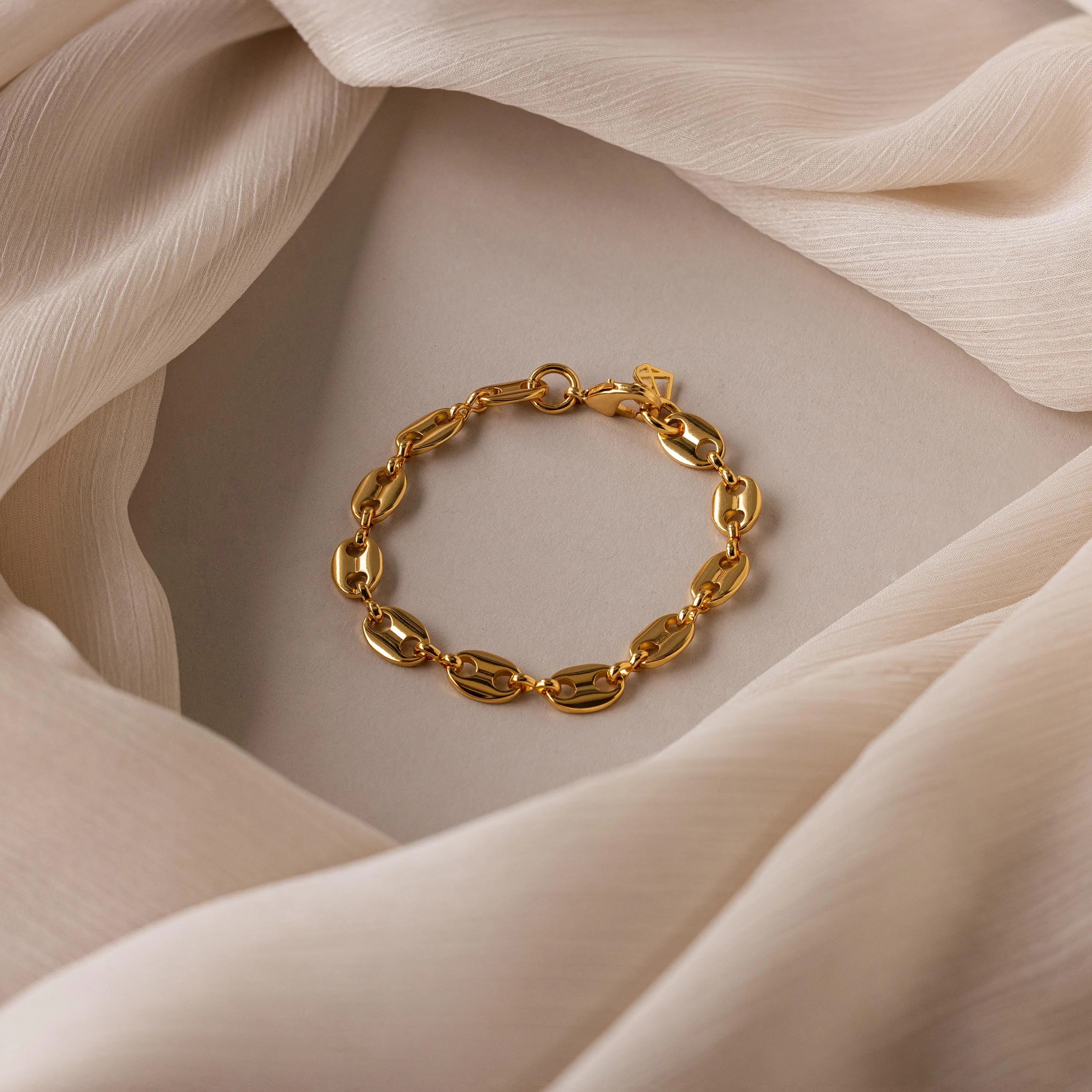 The Bold Mariner Chain Bracelet, featuring oversized links, is showcased on a softly folded neutral fabric background, highlighting its refined statement jewelry style.