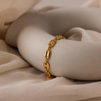 The Bold Mariner Chain Bracelet with oversized links is displayed on a smooth white sculptural object, set against beige fabric—a striking statement jewelry piece.