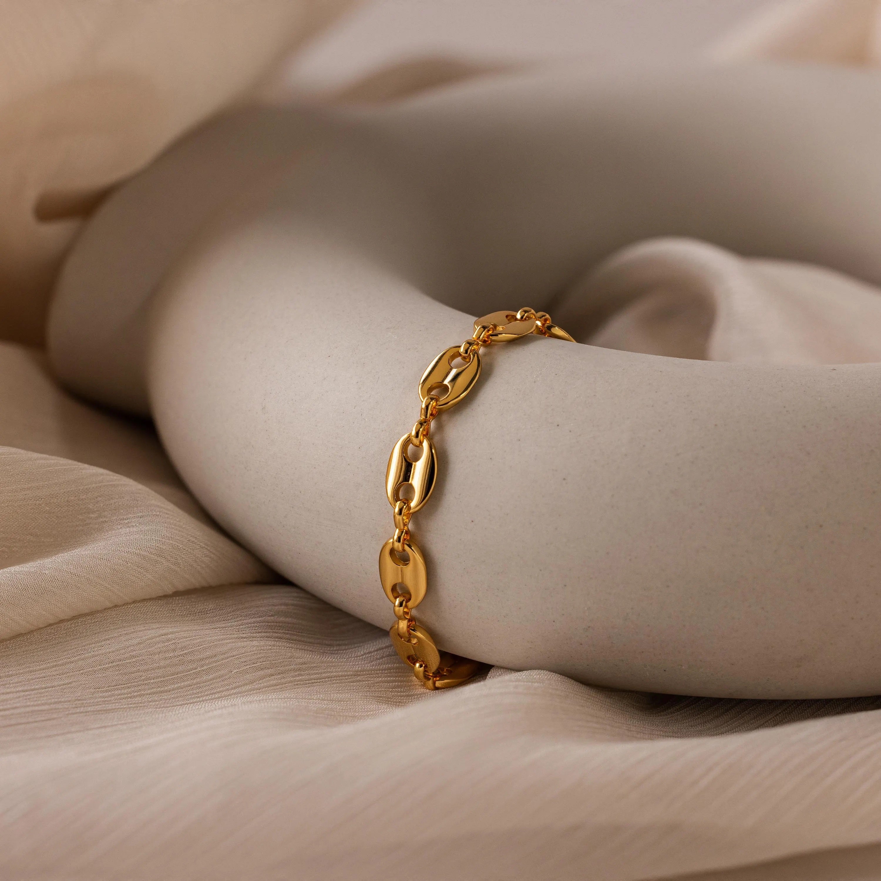 The Bold Mariner Chain Bracelet with oversized links is displayed on a smooth white sculptural object, set against beige fabric—a striking statement jewelry piece.