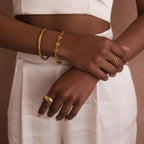 A person in white clothing wears statement jewelry: gold rings, a bracelet with oversized links, and the Bold Mariner Chain Bracelet on their wrists and fingers.