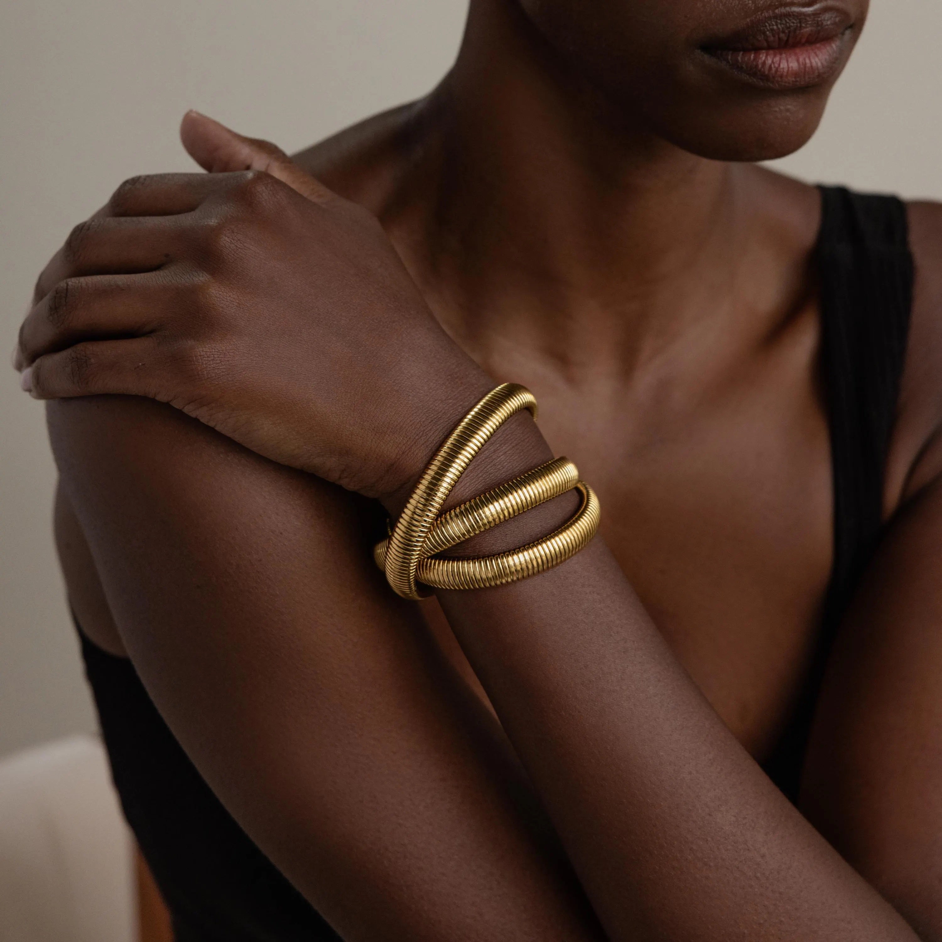 Wearing three chunky gold bracelets, including the Ribbed Infinity Bangle, a person crosses their arm over their chest to make a chic style statement.