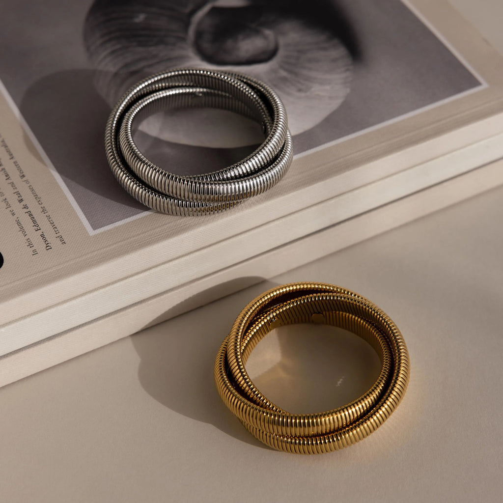 A Ribbed Infinity Bangle rests on a closed book with a monochrome shell cover photo, creating a stylish accessory display.