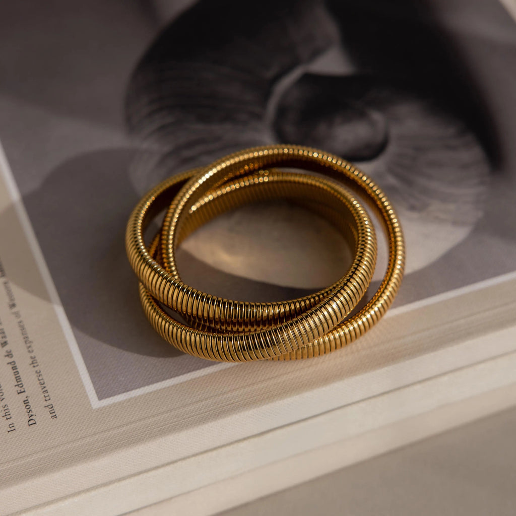 The Ribbed Infinity Bangle, stacked with two other interlocking bangles, sits elegantly on a book featuring a blurred black and white cover image.