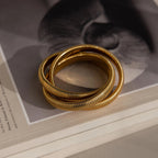 The Ribbed Infinity Bangle, stacked with two other interlocking bangles, sits elegantly on a book featuring a blurred black and white cover image.