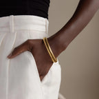 A person wearing white pants has their hand in their pocket, showcasing the Thick Snake Chain Bangle with a textured design.