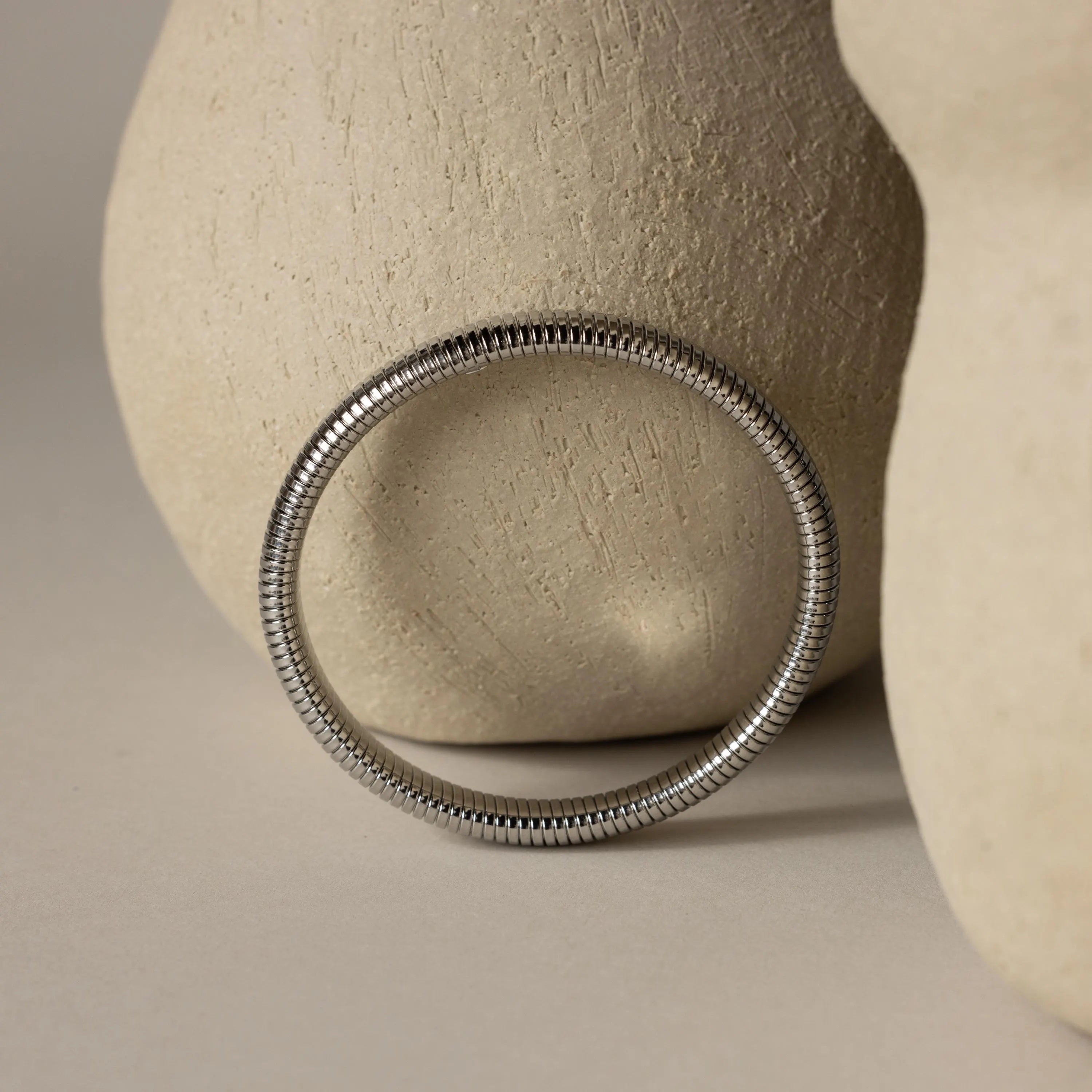 The Thick Snake Chain Bangle in silver is displayed beside two textured light beige ceramic vases on a neutral background.