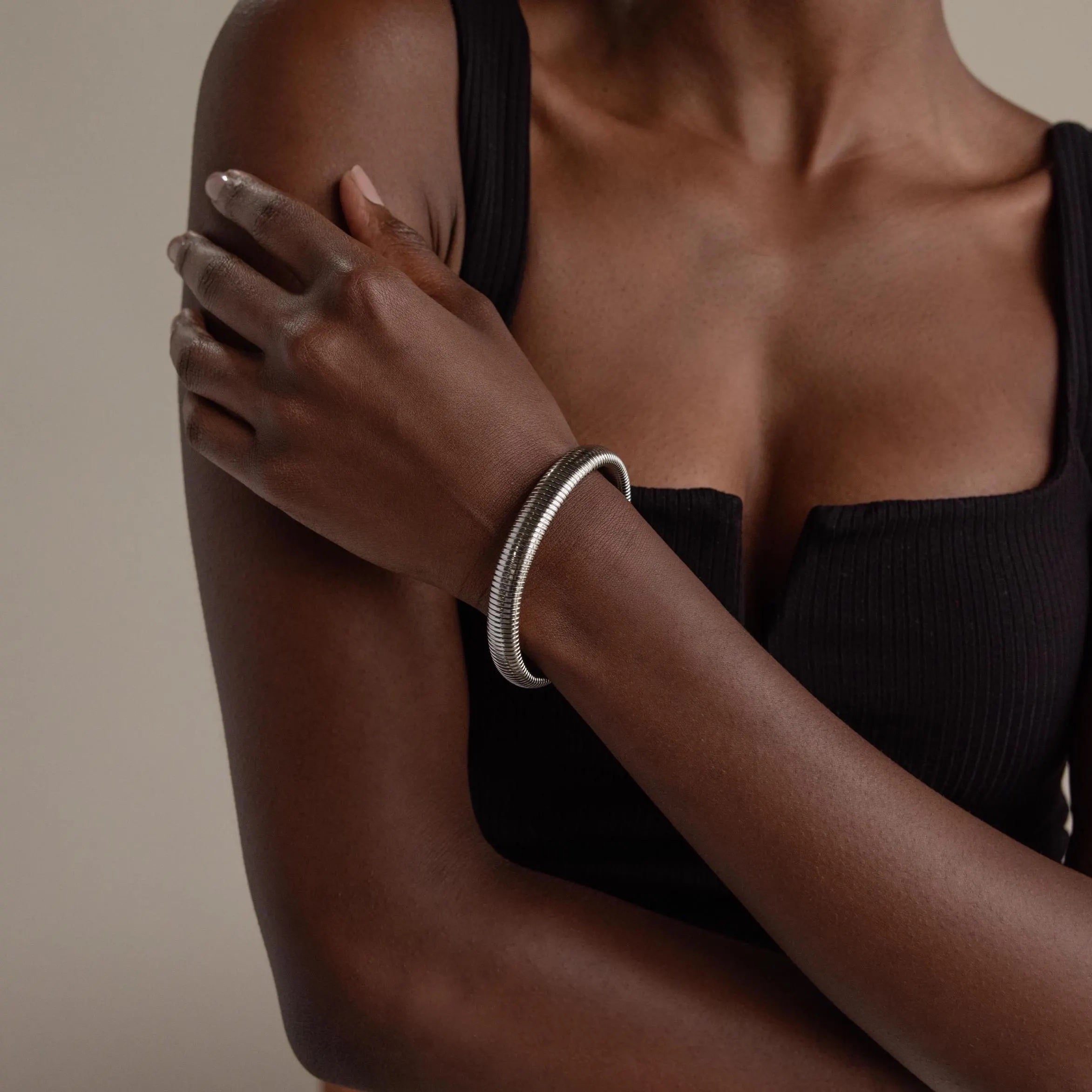 A woman in a black top wears the Thick Snake Chain Bangle, resting her hand on her upper arm against a neutral background.
