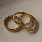 Three Thick Snake Chain Bangles with a ribbed, textured design are elegantly arranged on a light, textured surface.