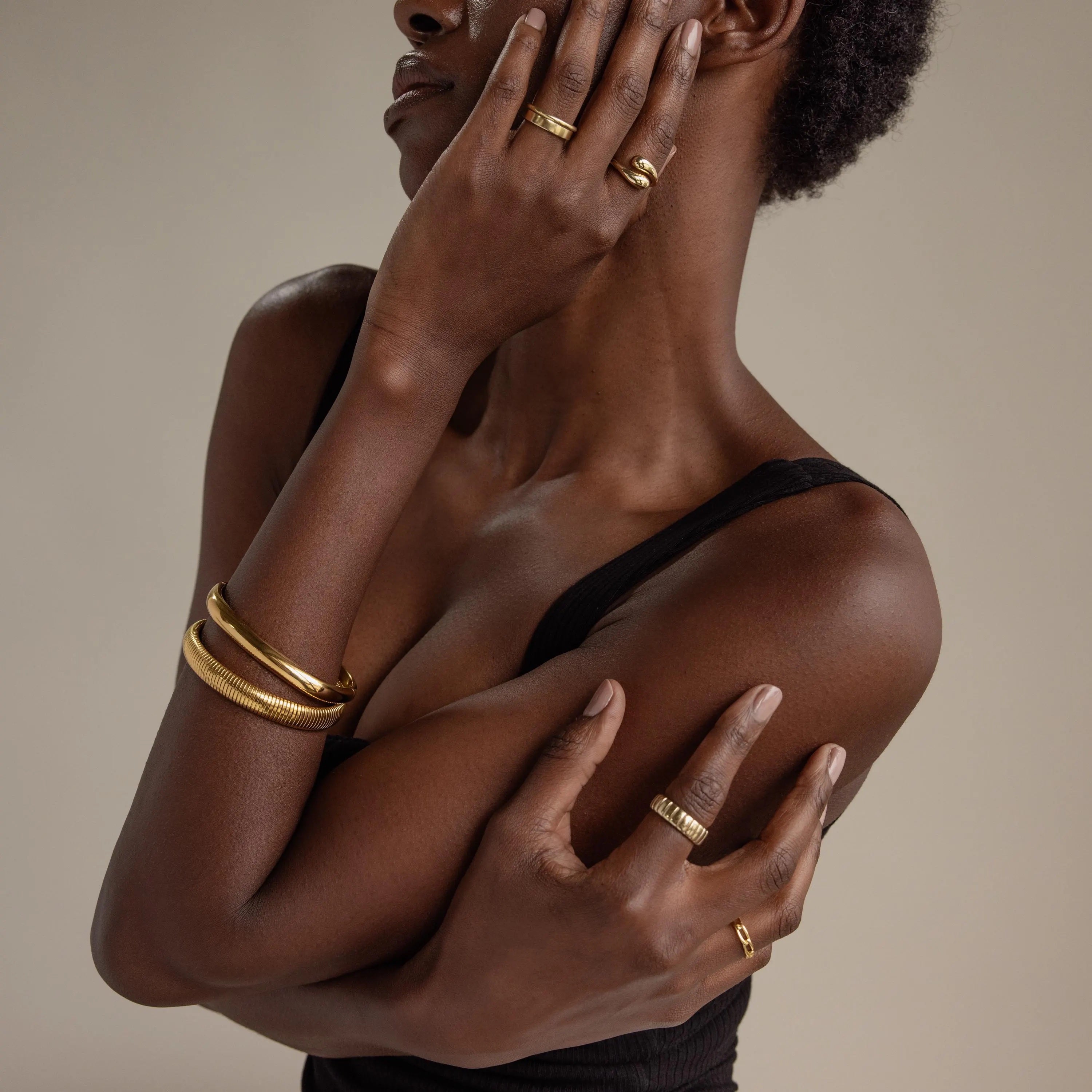 A woman wearing a black ribbed top showcases gold rings and the Thick Snake Chain Bangle, posing against a neutral background.