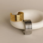 Ribbed Cuff Bracelets with elegant ridge detailing and grooved designs are displayed on a smooth white ceramic object.