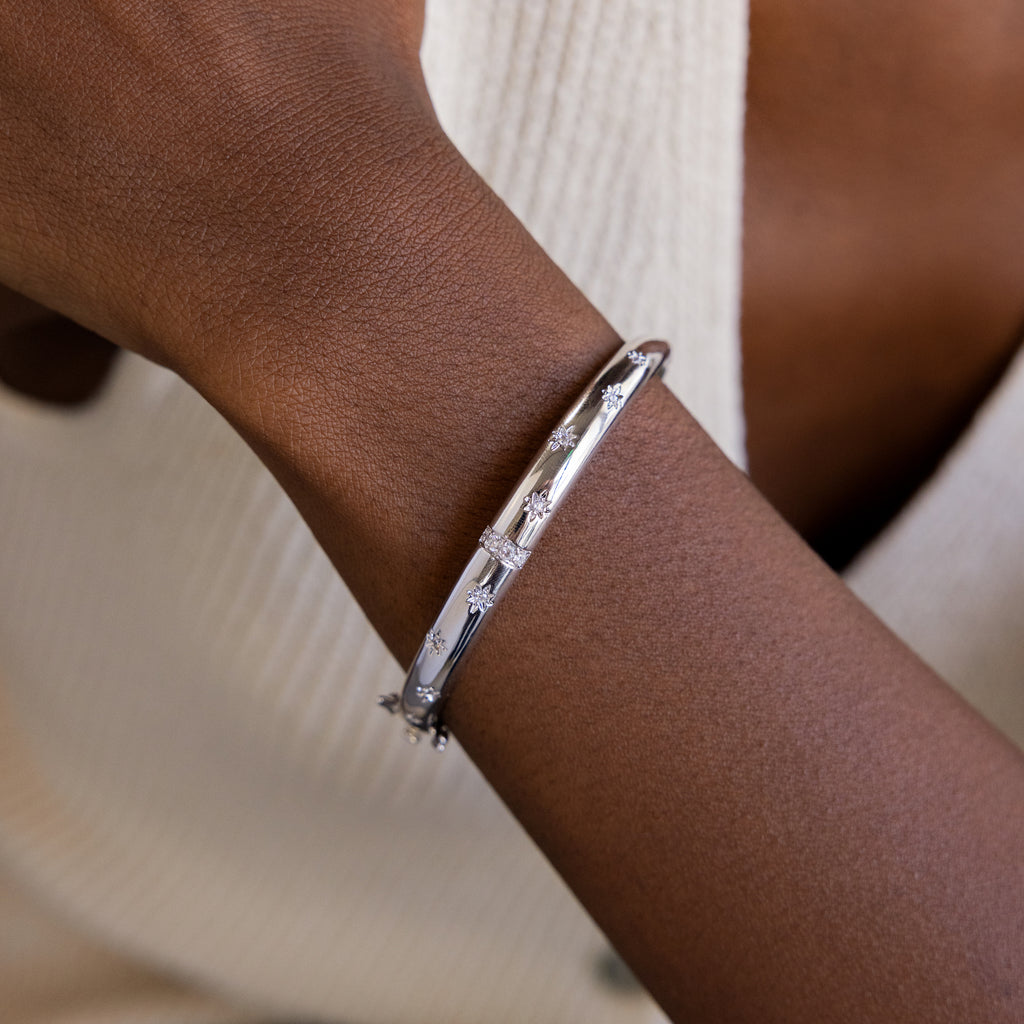 Silver North Star Diamond Bangle on women's wrist. The bangle is a dome shaped and features multiple North Star with Diamond CZ designs dotted around the bangle.