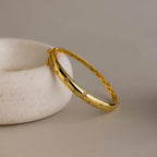 Flat lay of gold North Star Diamond Bangle resting at an angle against a beige ceramic dish