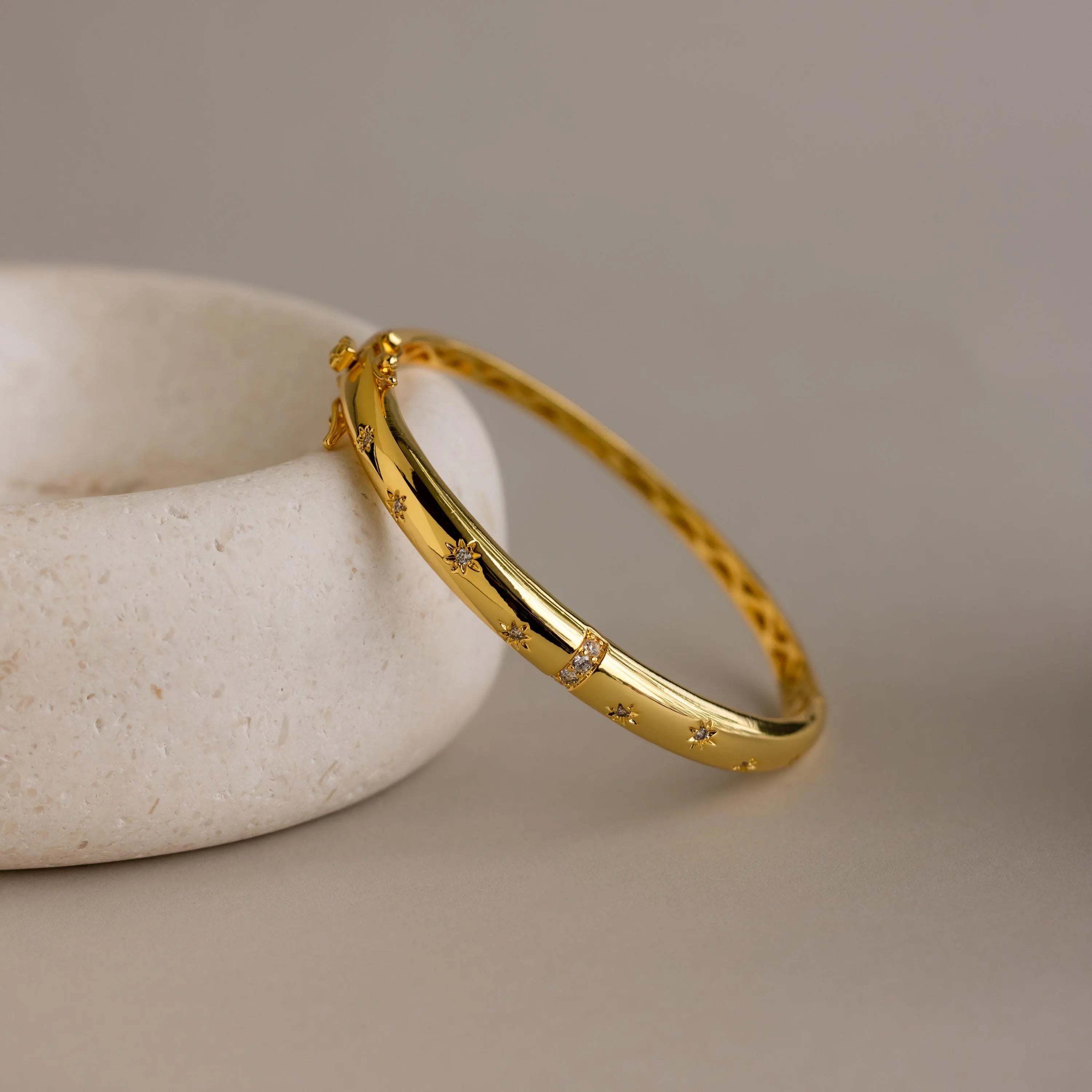 Flat lay of gold North Star Diamond Bangle resting at an angle against a beige ceramic dish