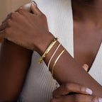 Gold North Star Bangle on women's wrist layered with a gold Diamond Tennis Bracelet and gold Herringbone Chain