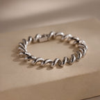 A Twisted Chain Bracelet with bold, gleaming links is displayed on a beige rectangular surface, exuding effortless glamour.