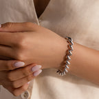 A person with manicured nails wears a beige button-up shirt and a Twisted Chain Bracelet in White Gold, its bold shining links adding effortless glamour.