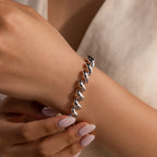 A hand adorned with a Twisted Chain Bracelet featuring bold, shining links, manicured nails, and a light-colored outfit captures effortless glamour.