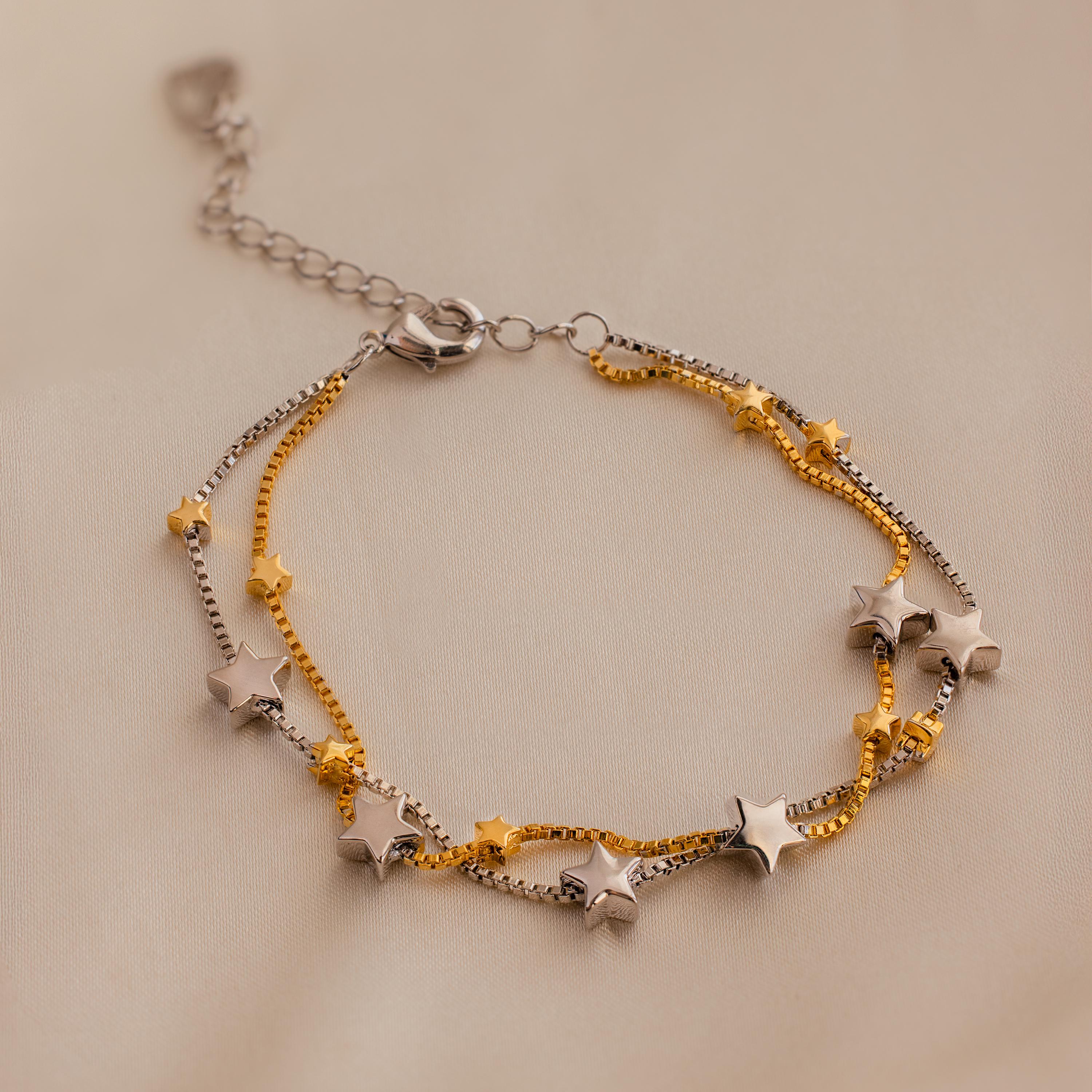 Close up of Mixed Metal Star Bracelet. The bracelet features a double box chain, the first chain is gold with alternating large white gold stars and small gold stars. The second chain is white gold with large white gold stars and small gold stars as well.