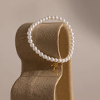 The Bow Pearl Bracelet in gold is draped over a sculptural, curved stand.