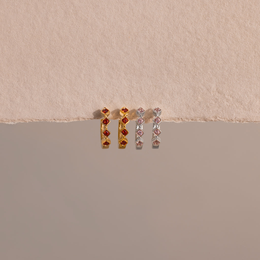Two pairs of Geometric Pink Tourmaline Huggies, one in gold and one in silver, displayed on a textured beige background—these rectangular gemstone earrings offer a modern update to classic birthstone jewelry.