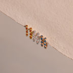 The Geometric Blue Zircon Huggies add a vibrant touch to your jewelry collection with their striking blue stones, shown against a beige textured background.