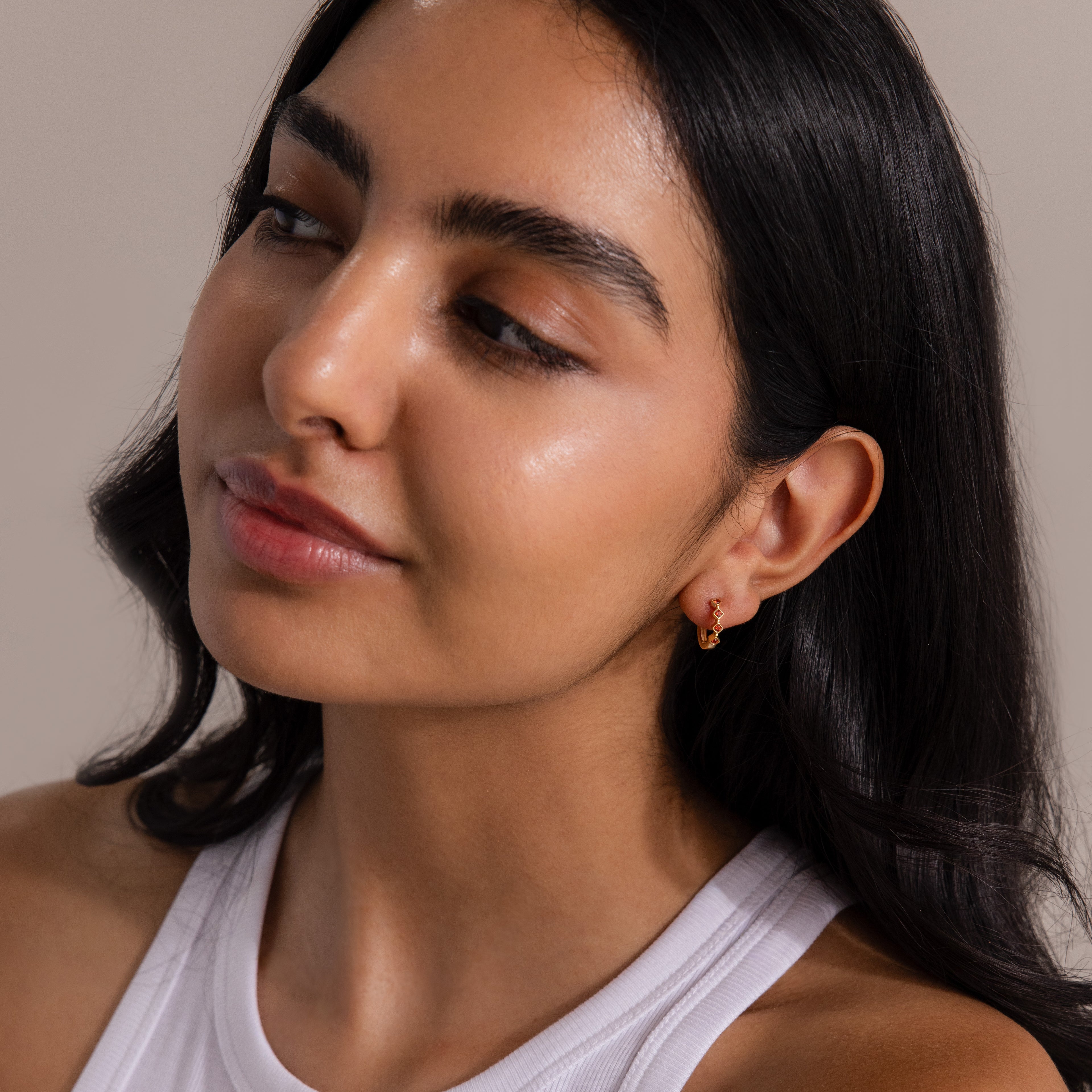 Woman with long dark hair wearing a white top and Geometric Blue Zircon Huggies, looking to the side.