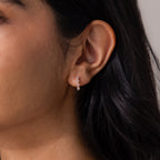 Close-up of a person with long dark hair wearing Geometric Birthstone Huggies—small, delicate silver earrings adorned with three gems and diamond accents for subtle sparkle.