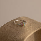 The Multiple Birthstone Bead Ring in Sterling Silver, featuring vibrant gemstone bands, sits atop a textured beige surface—a perfect choice for personalized jewelry.
