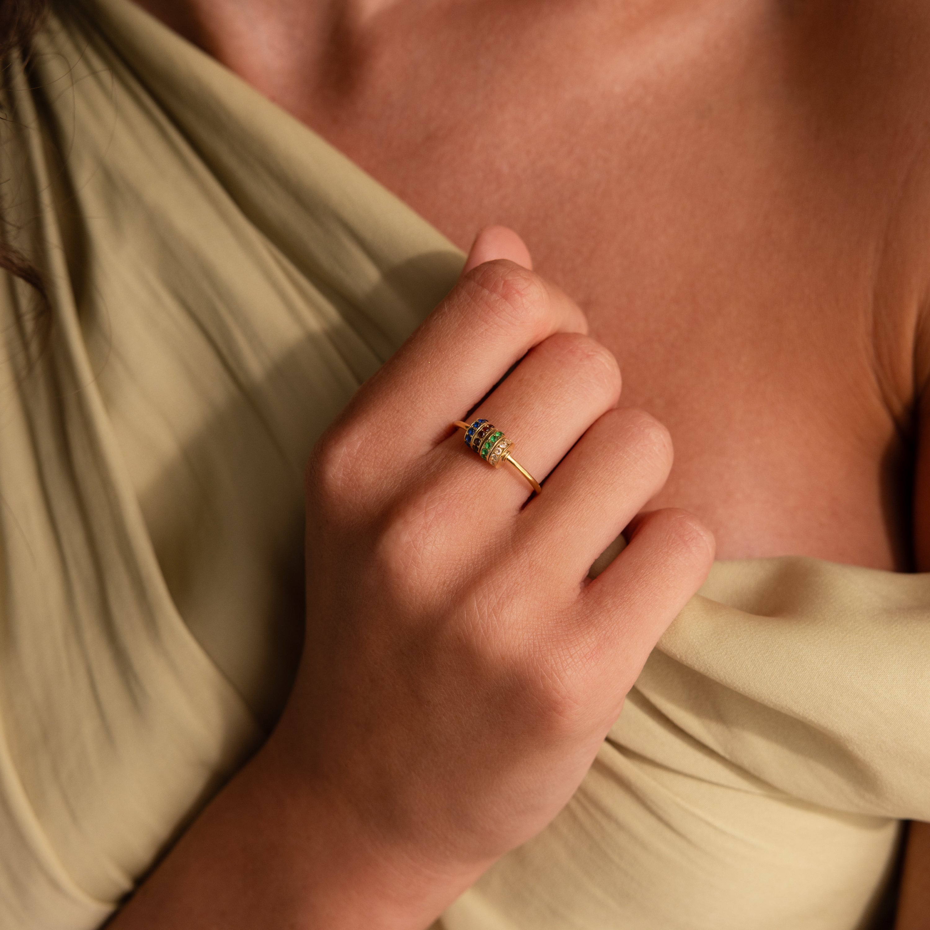 A hand adorned with the Multiple Birthstone Bead Ring rests on a beige off-shoulder dress, highlighting elegant personalized jewelry.
