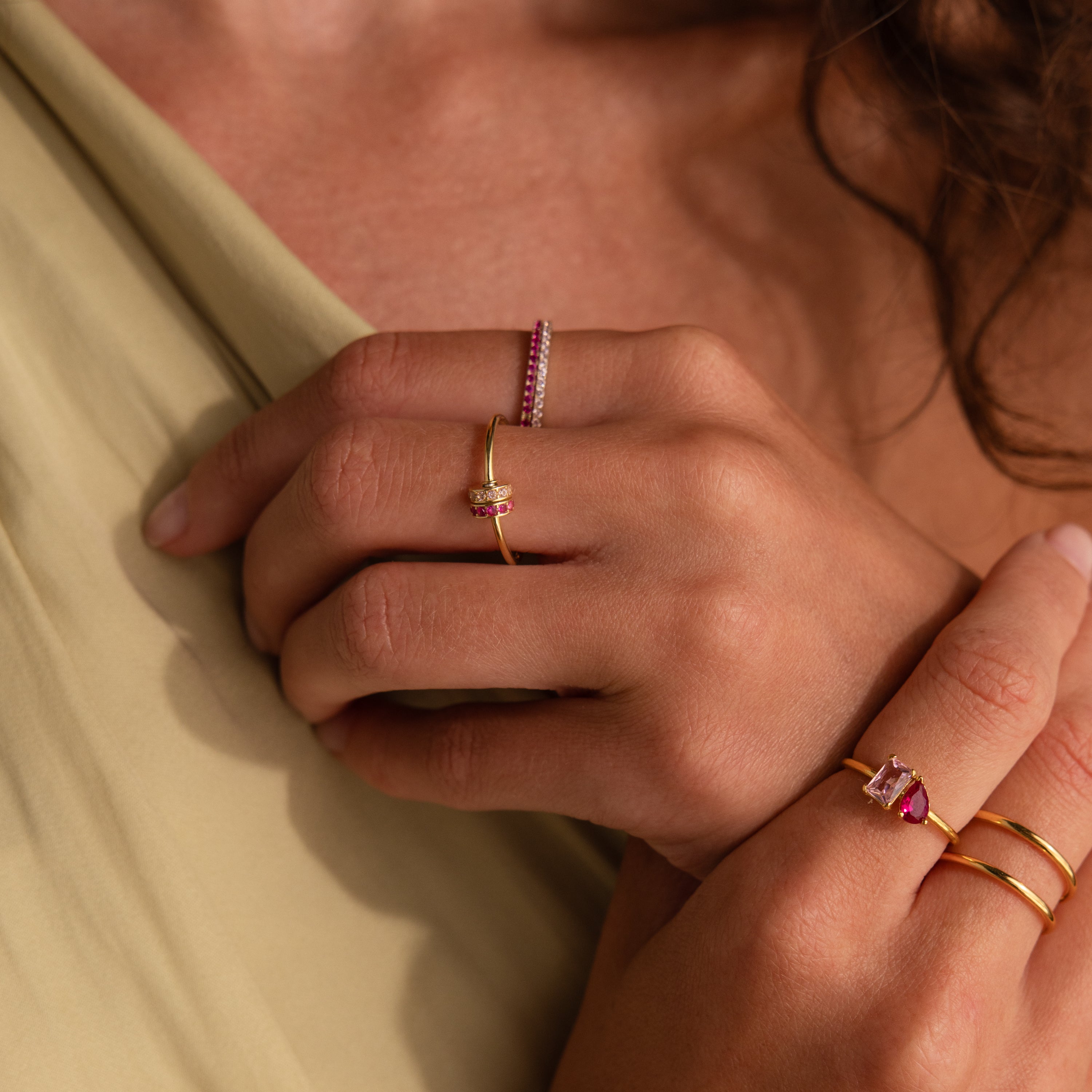 Close-up of hands wearing a Multiple Birthstone Bead Ring along with gold rings featuring pink and white stones, all stacked together on beige fabric.
