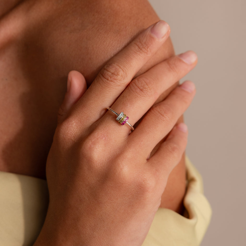 A hand with neatly manicured nails wears the Multiple Birthstone Bead Ring in Sterling Silver, featuring vibrant gemstones, resting gracefully on the chest.