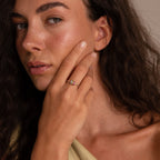 A woman with long dark hair touches her face, showcasing a Multiple Birthstone Bead Ring that highlights her personalized jewelry style with its elegant, stackable design.