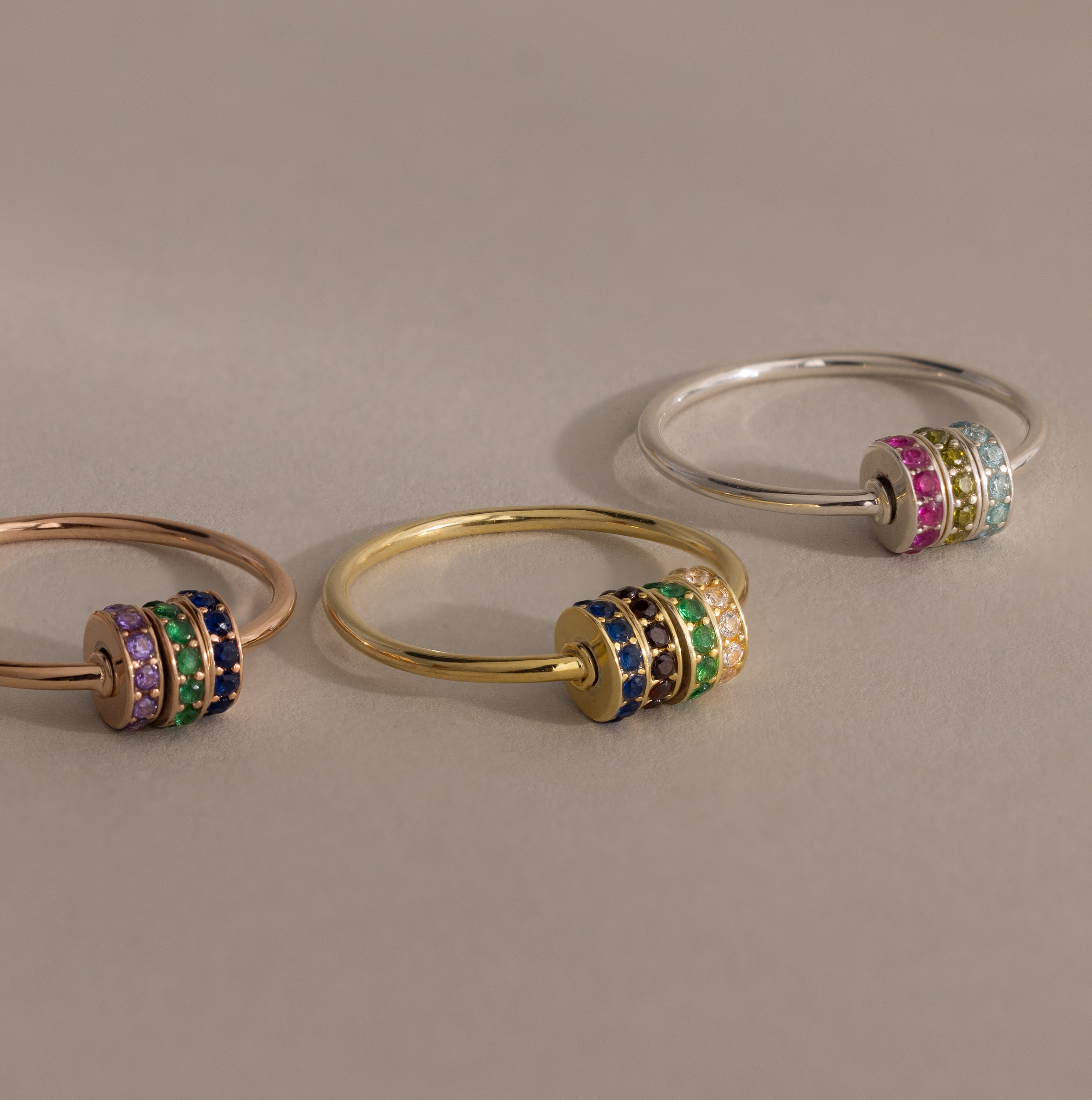 The Multiple Birthstone Bead Ring features stackable rose gold, yellow gold, and silver bands, each adorned with three vibrant gemstone-studded spinner bands for a customizable jewelry style.