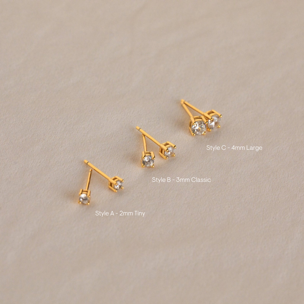 The Booker Diamond Studs Set features three pairs of lightweight gold earrings in small, medium, and large sizes on a light beige background—ideal for everyday wear.