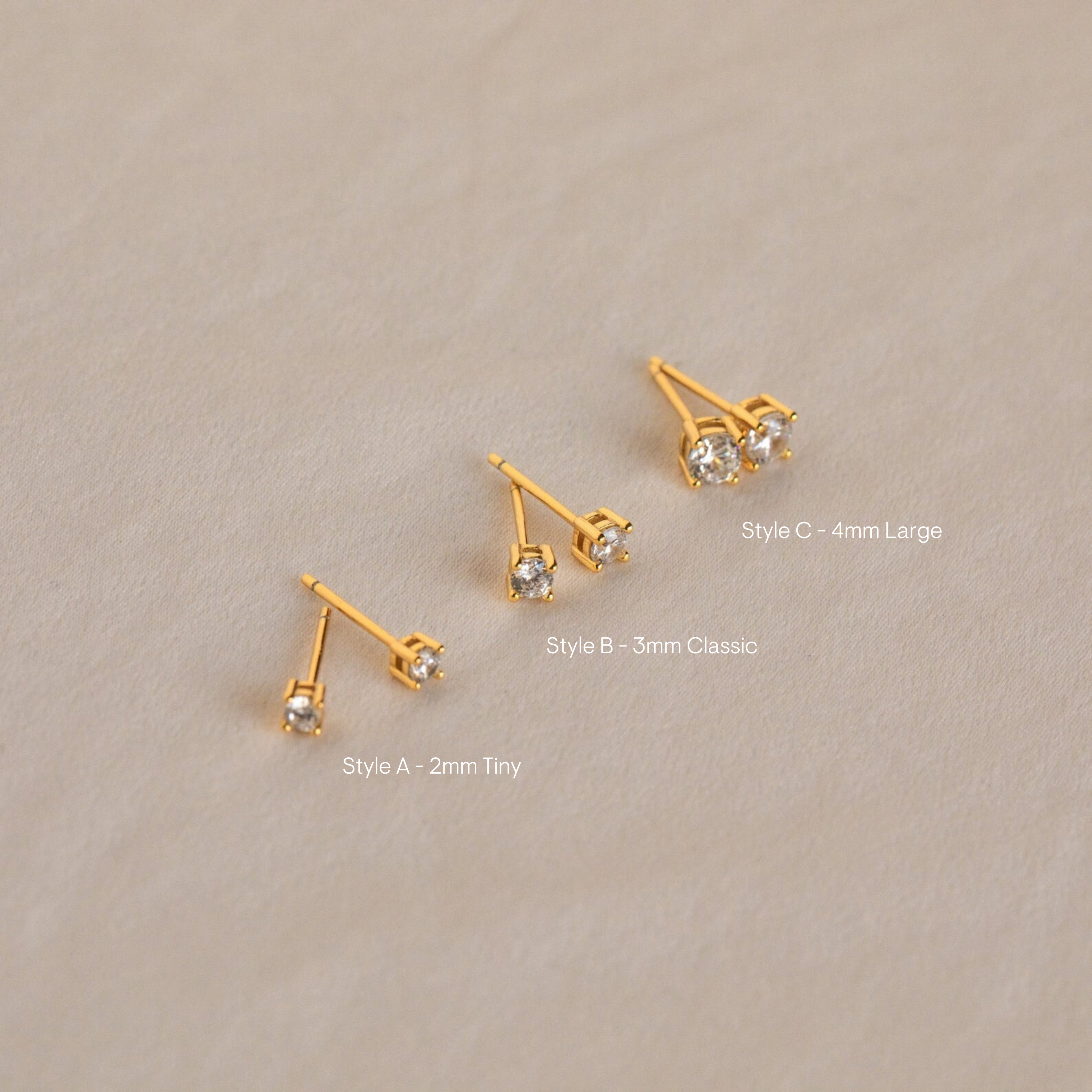 The Booker Diamond Studs Set features three pairs of lightweight gold earrings in small, medium, and large sizes on a light beige background—ideal for everyday wear.