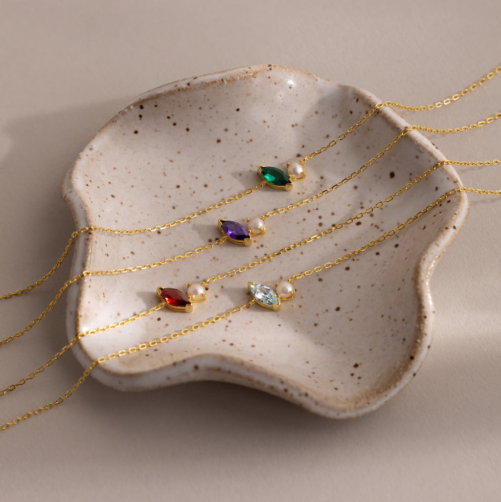 Four gold chain bracelets with colorful gems and pearls, including a stunning Marquise Opal & Pearl Bracelet, are elegantly displayed on a speckled ceramic dish—an ideal gift for someone special.