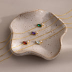Four gold chain bracelets with colorful gems and pearls, including a stunning Marquise Opal & Pearl Bracelet, are elegantly displayed on a speckled ceramic dish—an ideal gift for someone special.