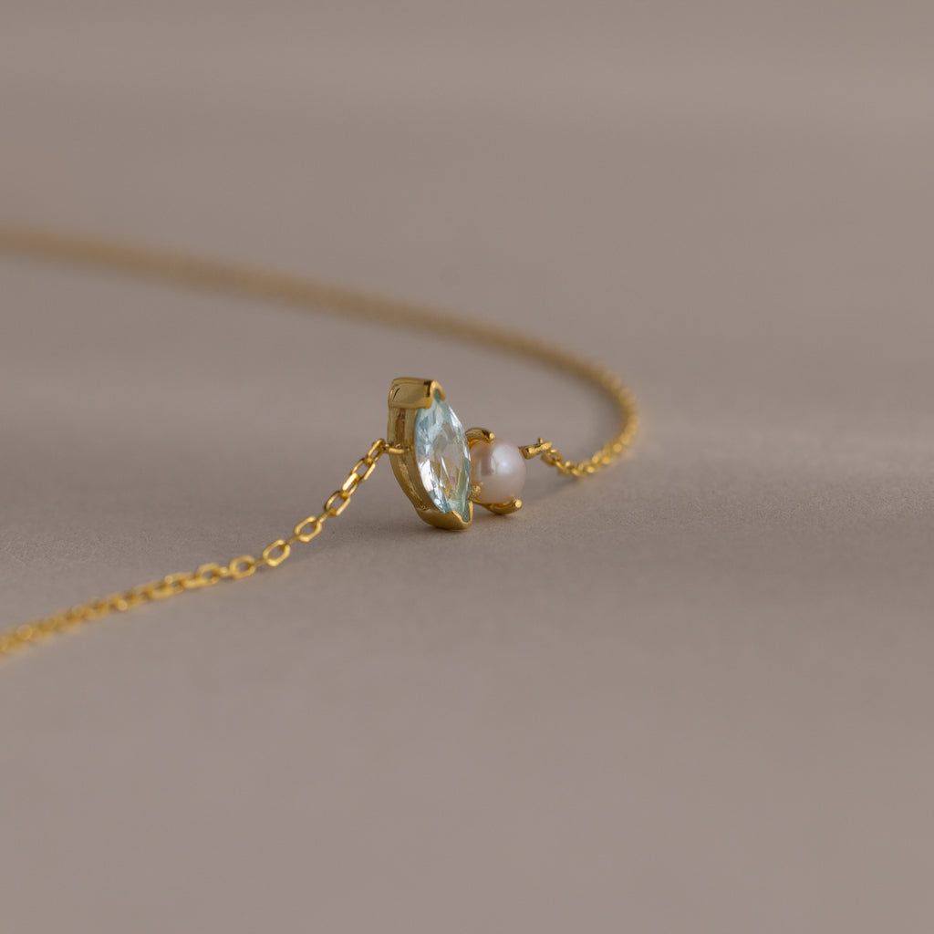A delicate gold chain bracelet featuring a marquise amethyst and a small pearl, perfect as a gift, set against a soft beige background.