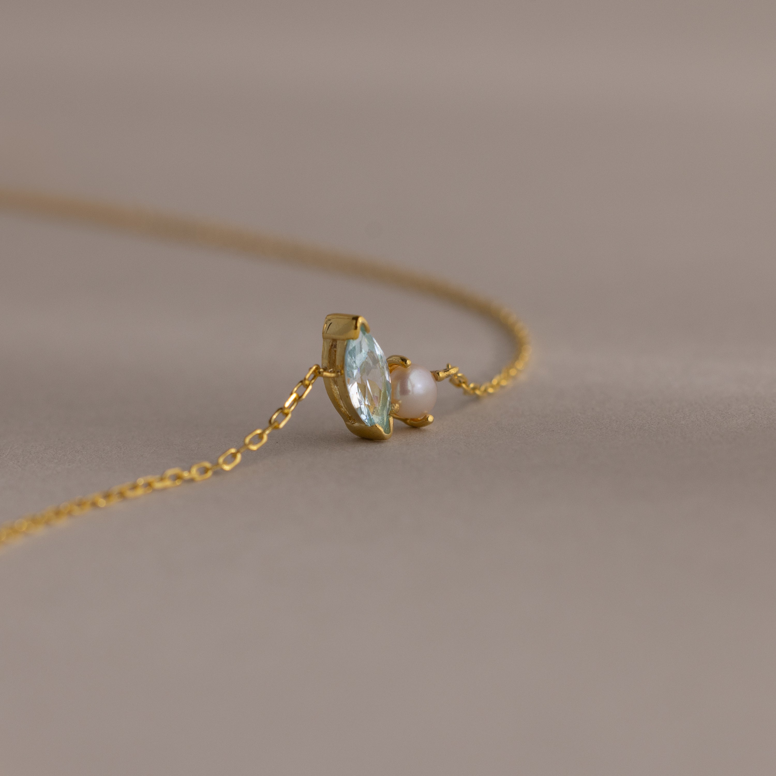 A delicate gold chain bracelet featuring a marquise amethyst and a small pearl, perfect as a gift, set against a soft beige background.