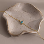 The Marquise Blue Zircon & Pearl Bracelet, featuring a blue gem and pearl, is displayed on a speckled wavy ceramic dish—a perfect gift for someone special.