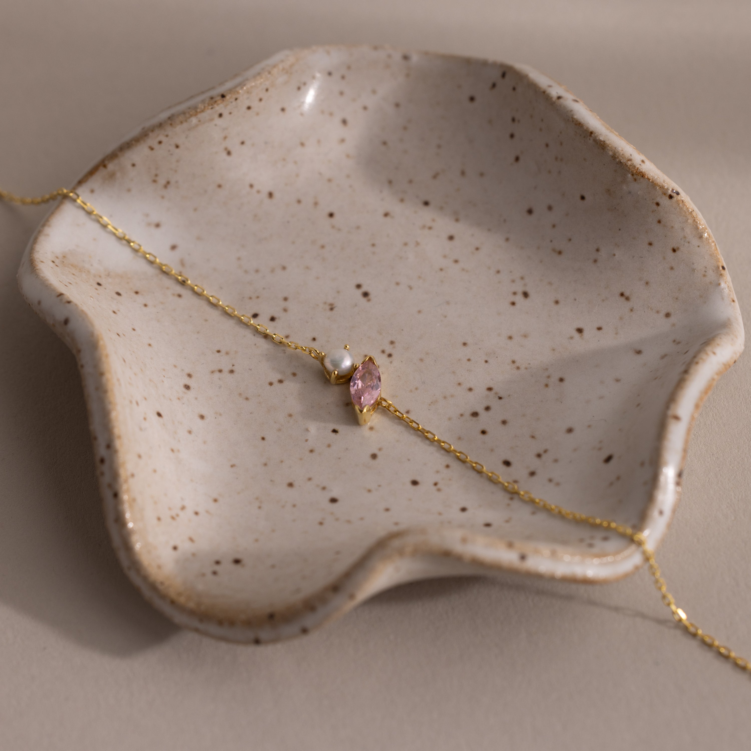 The Marquise Pink Tourmaline & Pearl Bracelet, shown on a wavy-edged speckled ceramic dish, makes a perfect gift for someone special.
