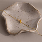 The Marquise Topaz & Pearl Bracelet features a gold chain, pearl accents, and a gold leaf charm—an elegant gift inspired by the timeless beauty of marquise birthstones. Displayed on a speckled ceramic dish.