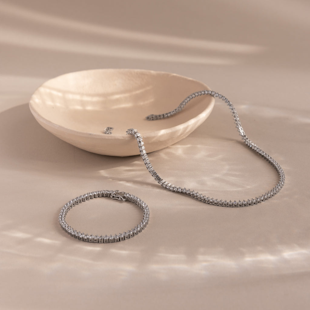 3-Prong Diamond Tennis Necklace & Bracelet Set in White Gold, both with classic 3-prong settings, displayed on a beige surface beside a shallow ceramic dish.